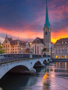 a bridge that has a clock tower in the background and buildings on both sides at sunset