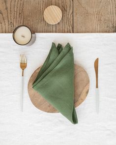 a place setting with green napkins and silverware on a wooden plate next to a candle