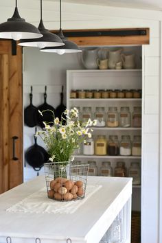 a kitchen island with flowers and eggs in a basket sitting on top of it next to hanging lights