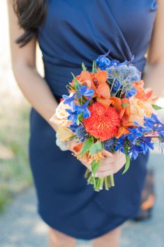 a woman in a blue dress holding a bouquet of orange, blue and white flowers