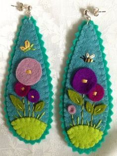 two pieces of felt with flowers are hanging from hooks on a white surface, one is green and the other is purple