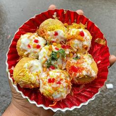 a hand holding a red bowl filled with food