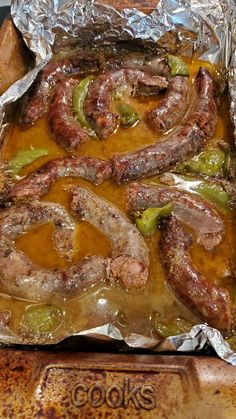 sausages and peppers wrapped in foil on top of a grilling pan filled with sauce