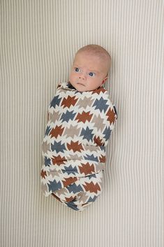 a baby wrapped in a blanket laying on top of a white bed next to a wall