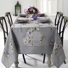 the table is set with two place settings and purple flowers in vases on it