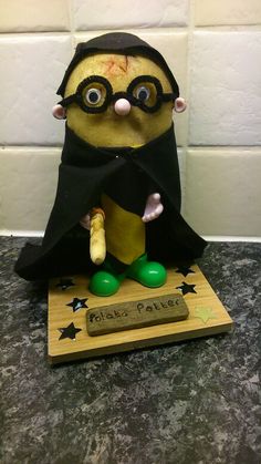 a small figurine is dressed in a black cape and green rubber boots, standing on top of a wooden plaque