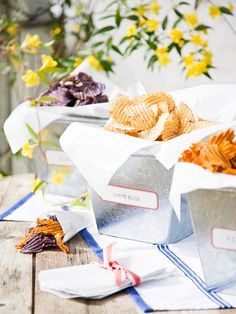 two silver containers filled with chips sitting on top of a wooden table next to flowers