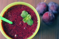 a green cup filled with red liquid next to some blueberries on a wooden table