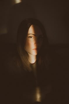 a woman is sitting in the dark with her head turned to the side and light shining on her face