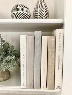 some books are sitting on a shelf next to a potted plant and two vases