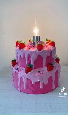 a pink birthday cake with strawberries on it and a lit candle in the middle