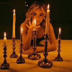 a woman sitting in front of candles with her hands on the table and looking at the camera