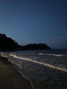 an empty beach at night with waves coming in to shore and trees on the other side