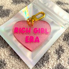 a pink heart shaped keychain with the words, rich girl era on it