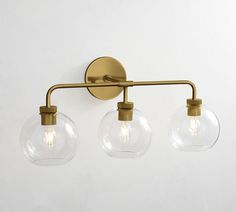 three clear glass globes hang on an antique brass wall light