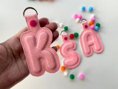 a hand holding a pink keychain with the letters b and c on it