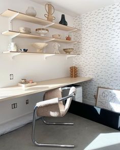 a chair sitting in front of a desk with shelves on the wall and vases behind it