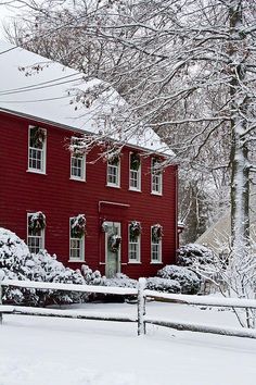 a red house is covered in snow and surrounded by trees, shrubs, and bushes