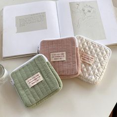 three small zippered pouches sitting on top of a table next to an open book