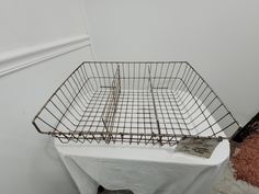 a wire basket sitting on top of a white tablecloth covered floor next to a wall