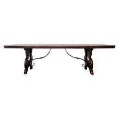 a long wooden table with two metal hooks on it's legs and an iron bar attached to the top