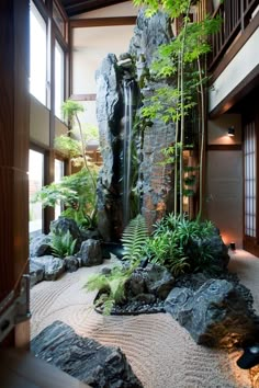 an indoor garden with rocks, plants and water features in the center of the room