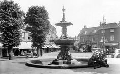 an old black and white photo of a fountain in the middle of a town square