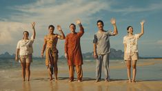 four people standing on the beach with their arms in the air and one person holding his hands up