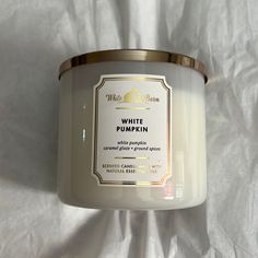 a candle that is sitting on a white sheet with a gold rim and label reading white pumpkin