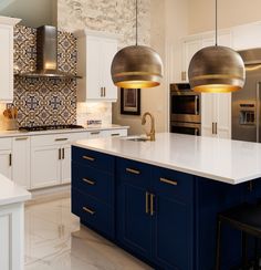 a large kitchen with white cabinets and blue island in the center, gold pendant lights hanging from the ceiling