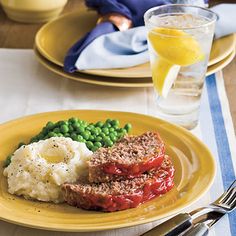 a plate with meatloaf, mashed potatoes and peas next to a glass of orange juice