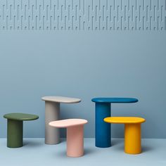 three different colored stools sitting in front of a blue and gray wall with vertical lines on it