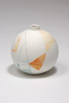 a white vase with an orange and blue design on the top is sitting in front of a gray background