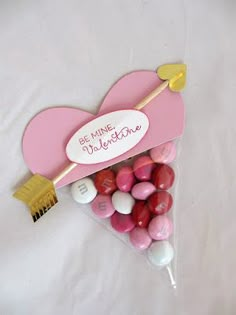 a pink heart shaped box filled with candies on top of a white tablecloth