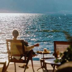 a man sitting on top of a wooden chair next to the ocean in front of him