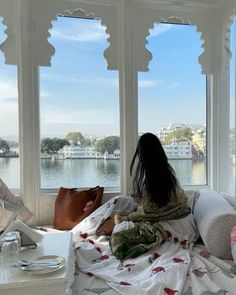 a woman sitting on top of a bed in front of a window next to a lake