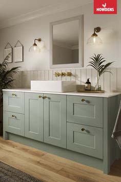 an image of a bathroom setting with light green cabinets and white counter tops, wood flooring