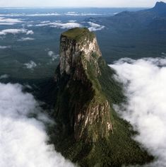 an aerial view of the top of a mountain in the sky with clouds surrounding it