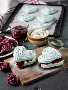 some heart shaped sandwiches are on a cutting board next to other desserts and bowls