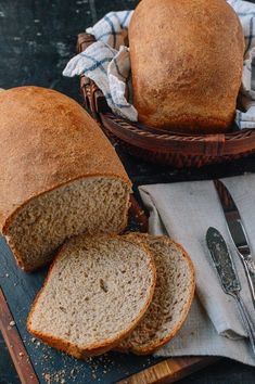 two loaves of bread sitting on top of a cutting board next to a knife and fork