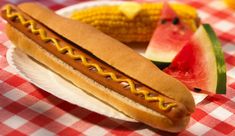 a hot dog sitting on top of a bun next to watermelon and corn