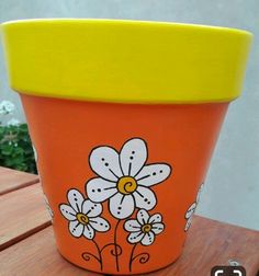 an orange flower pot sitting on top of a wooden table with flowers painted on it