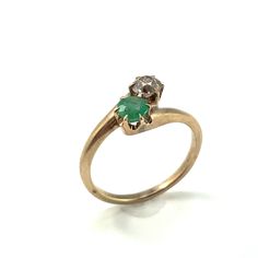 a gold ring with an emerald and two diamonds on the top, sitting on a white surface