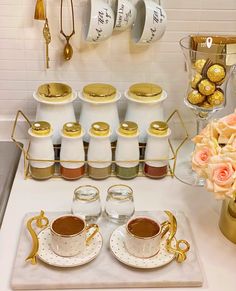 two cups of coffee sit on a tray next to some gold and white teacups