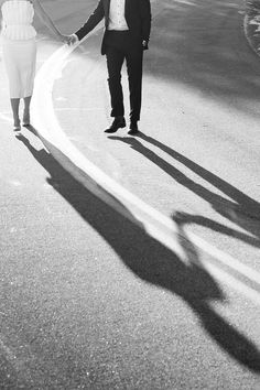 a man and woman holding hands while walking down the street with their shadow on the ground