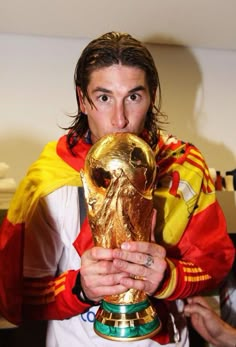 a man holding a soccer ball in front of his face while wearing a red, yellow and white shirt