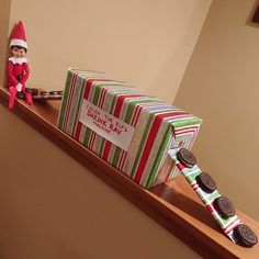 an elf is sitting on top of a shelf next to a box with cookies in it