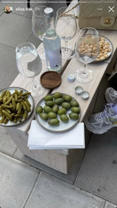 a table with plates of food and glasses on it next to a purse, wine glass, and water bottle