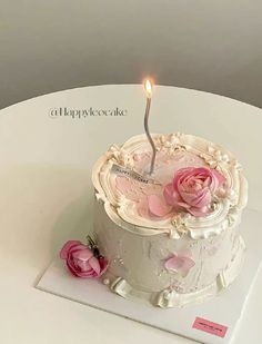 a white cake with pink flowers on it and a single lit candle in the middle