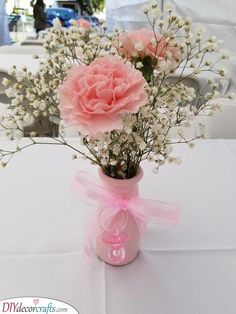 a vase filled with pink flowers on top of a white table covered in tables cloths